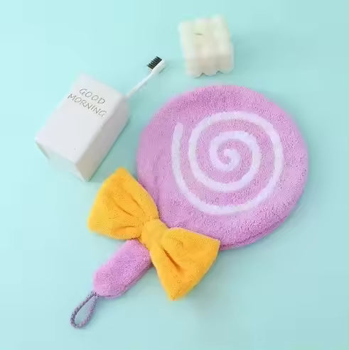 Purple and yellow lollipop design bathroom towel with a bow next to a toothbrush and soap holder