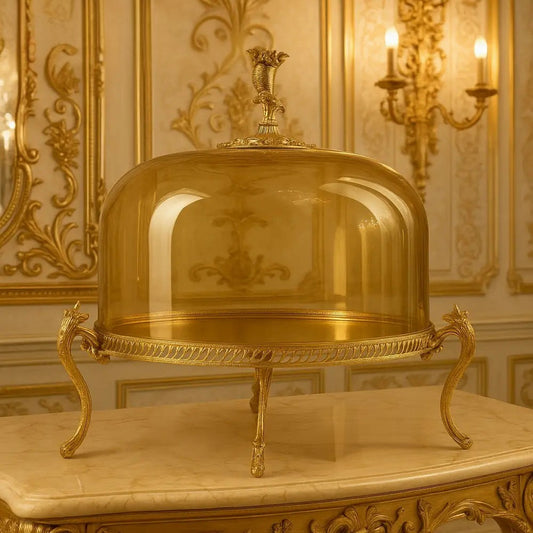 Elegant amber glass cake cloche with ornate gold stand and decorative handle on marble table