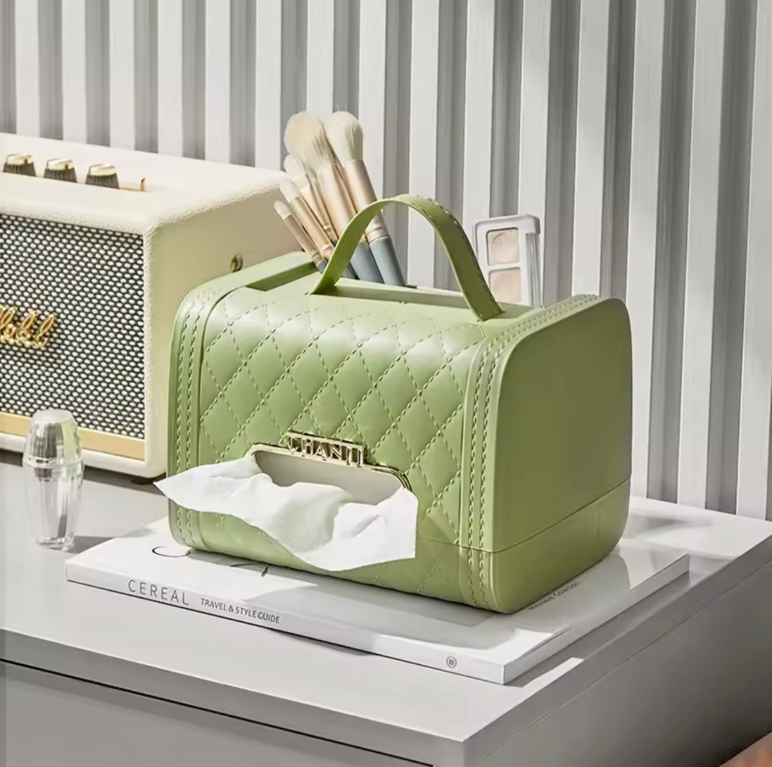Green quilted handbag tissue box holder with handle on a table next to makeup brushes and a radio