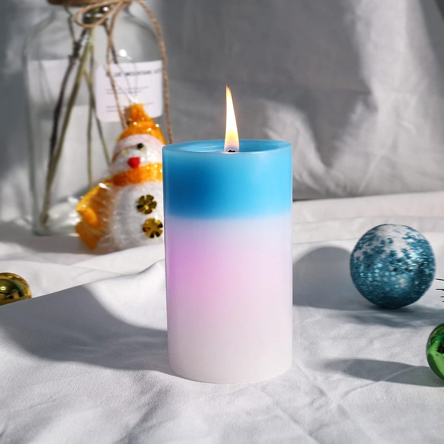 Lit blue and white gradient magic wax mood candle on white cloth with holiday decor background