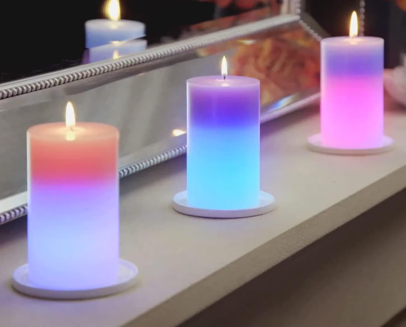 Three lit magic wax mood candles in gradient colors placed on a white surface near a mirror