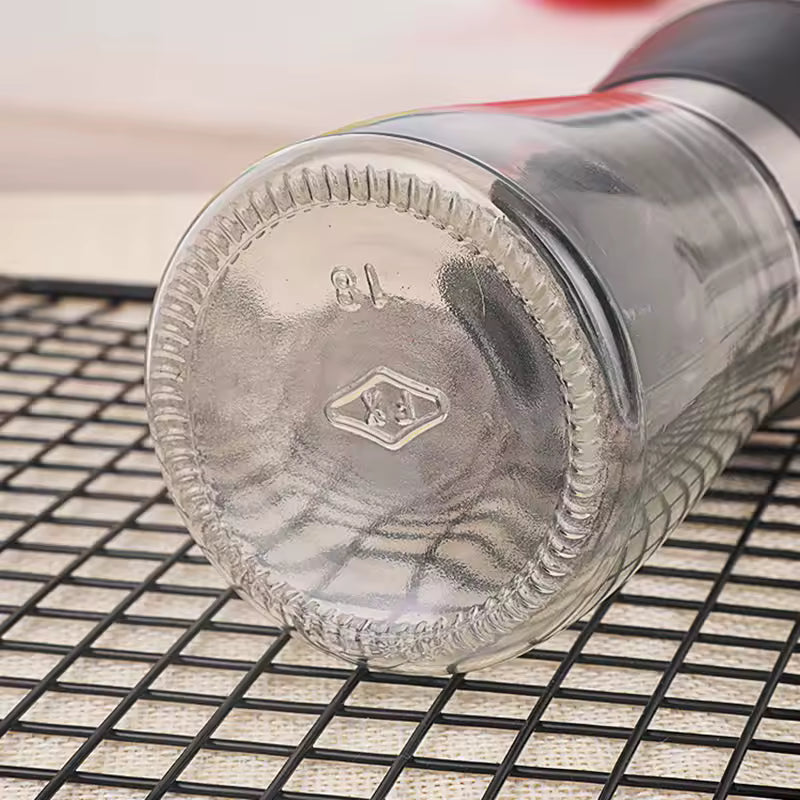 Clear glass manual salt and pepper grinder lying on a black cooling rack surface