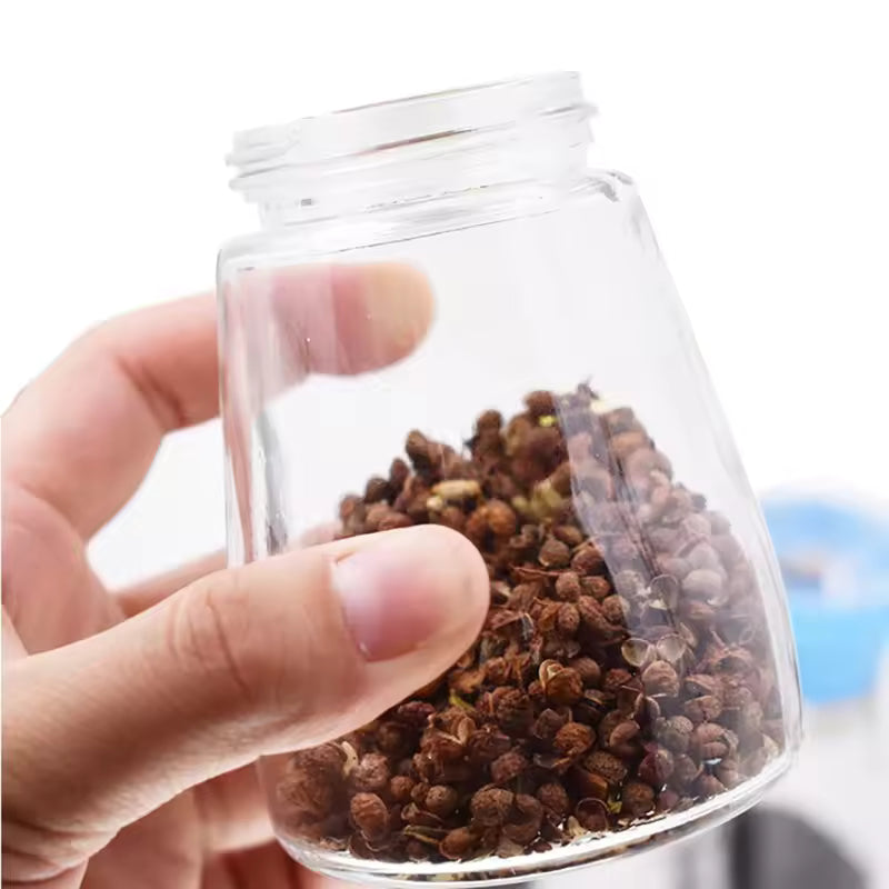 Hand holding clear glass manual salt and pepper grinder filled with peppercorns from Clarify pk