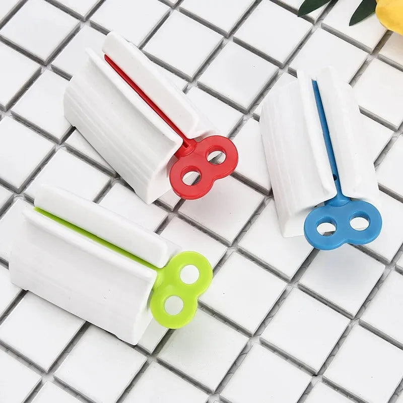 Clarify.pk manual toothpaste squeezer with white body and red blue green handles on tiled surface