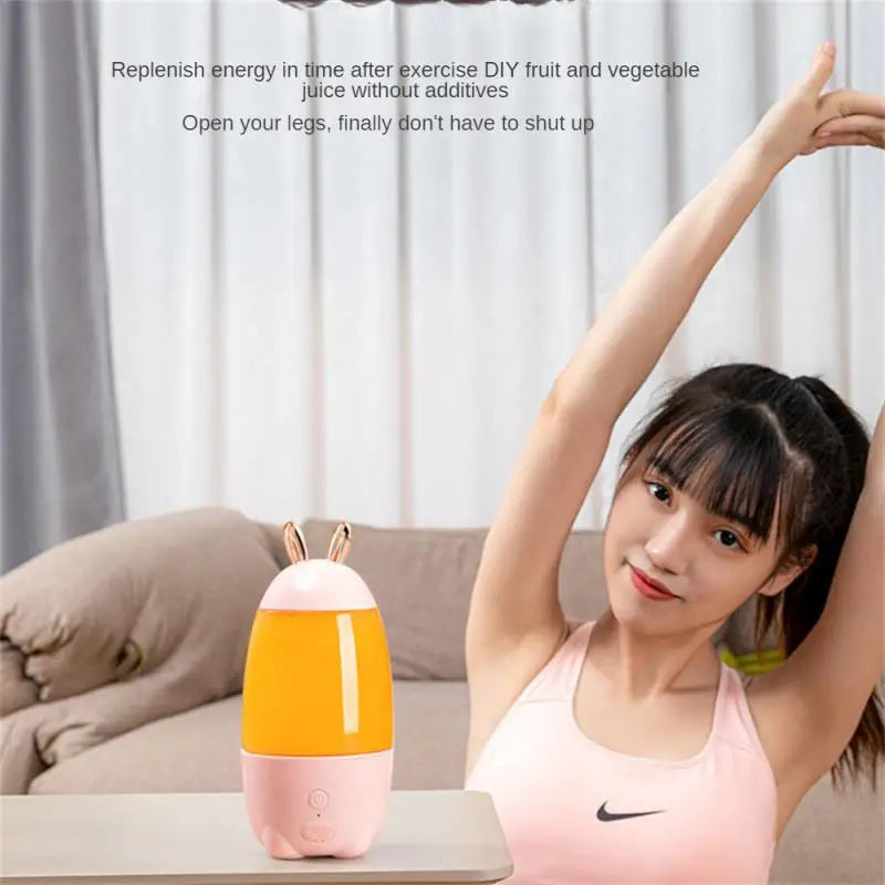 Portable electric juicer in pink and orange with bunny ears beside a woman stretching after exercise