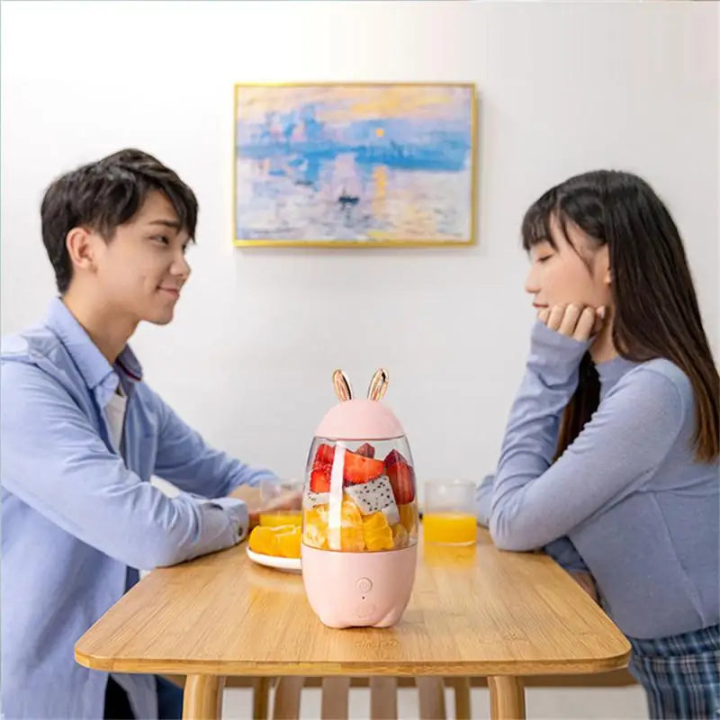 Clarify.pk portable electric juicer in pink with bunny ears filled with fresh fruit on dining table