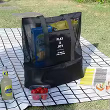 Black mesh beach bag with pockets filled with summer essentials on picnic blanket outdoors