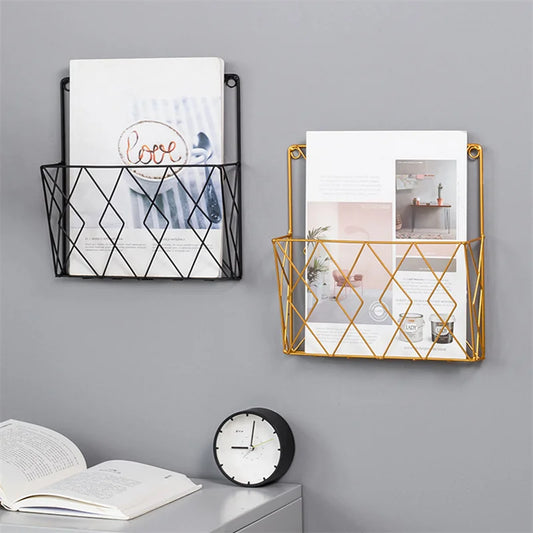 Black and gold metal wall mounted rack holding magazines on a gray wall above a desk with clock and open book