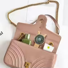 Mini fan with phone stand inside a pink handbag alongside perfume and small card