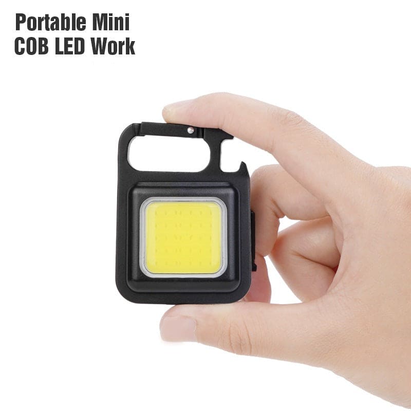 Clarify.pk portable mini LED flashlight keychain held between fingers with black frame and yellow light panel
