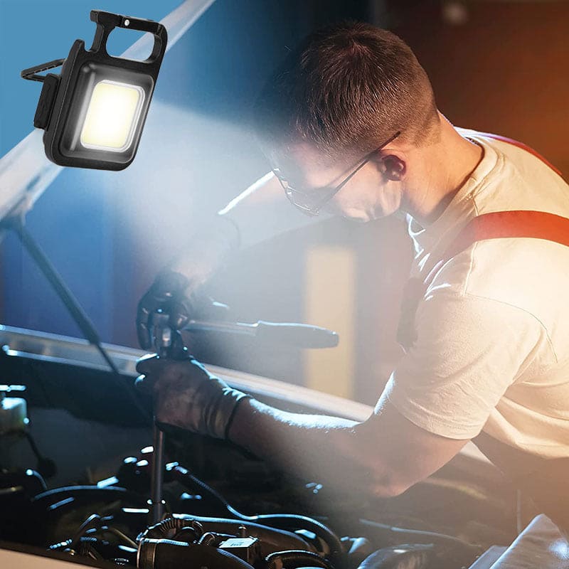 Mini LED flashlight keychain shining bright light on a mechanic working under a car hood