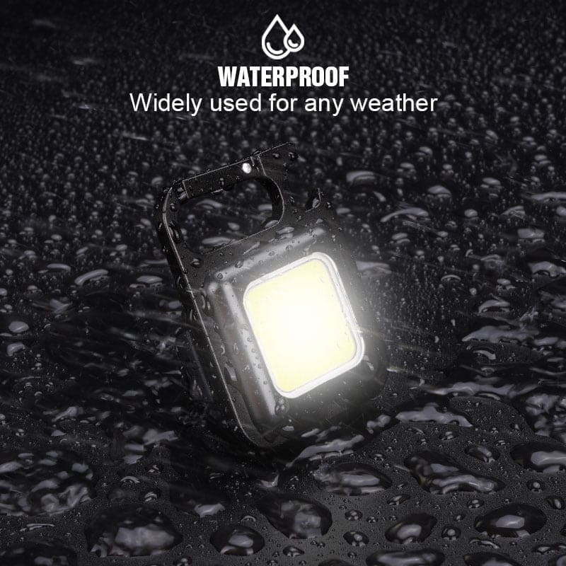 Waterproof mini LED flashlight keychain shining brightly with water droplets on black surface