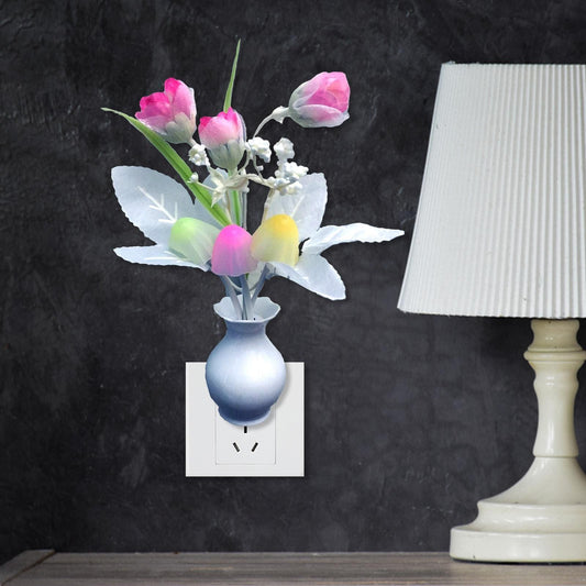 Mini LED night lamp shaped like colorful flowers in a vase plugged into a wall outlet next to a white table lamp