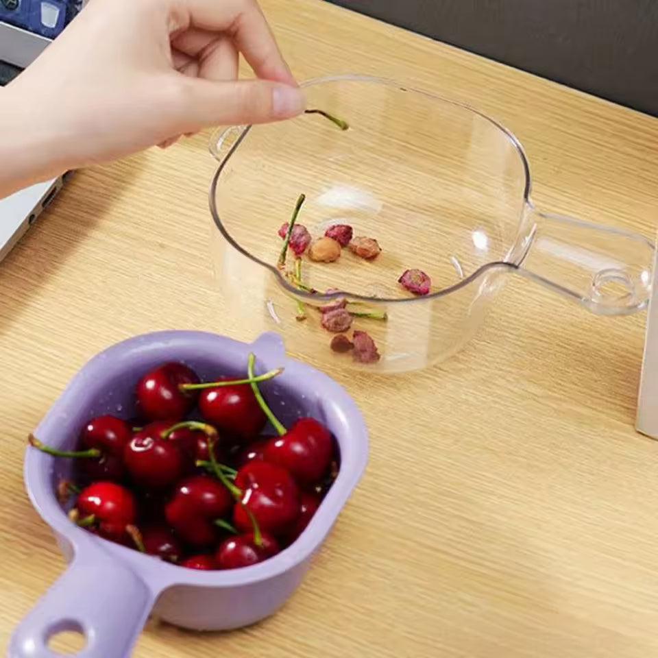 Clear plastic multi-functional drain basket with handle next to purple basket holding fresh cherries