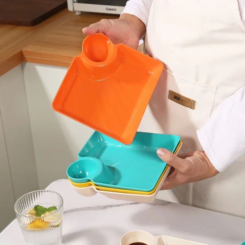Clarify.pk multipurpose snack plates with sauce compartment in orange, teal, and yellow held by a person