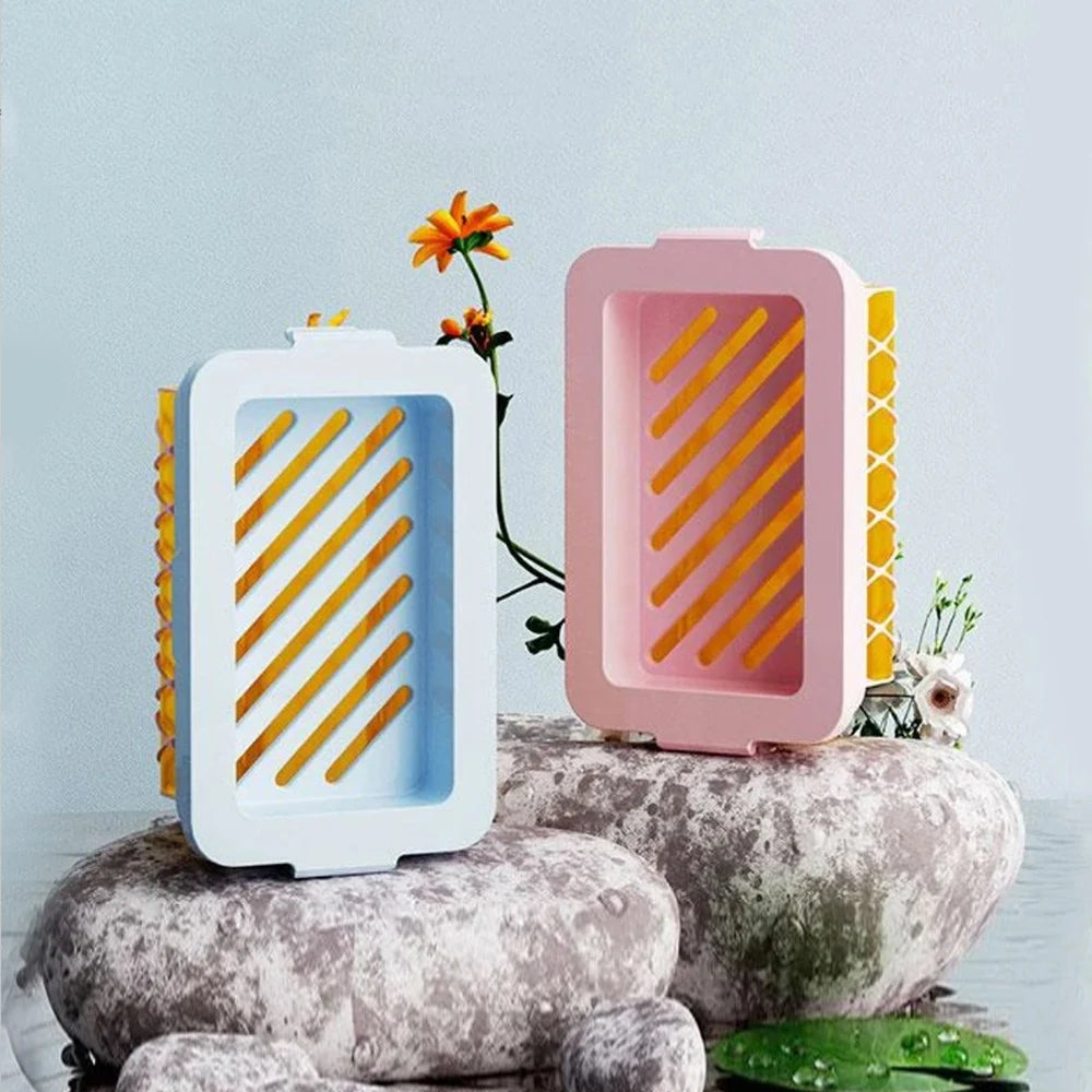 Blue and pink non slip soap holder with yellow drainage slats displayed on decorative stones