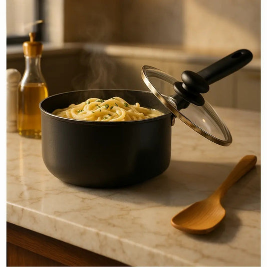 Black nonstick saucepan with glass lid cooking pasta on marble countertop with wooden spoon