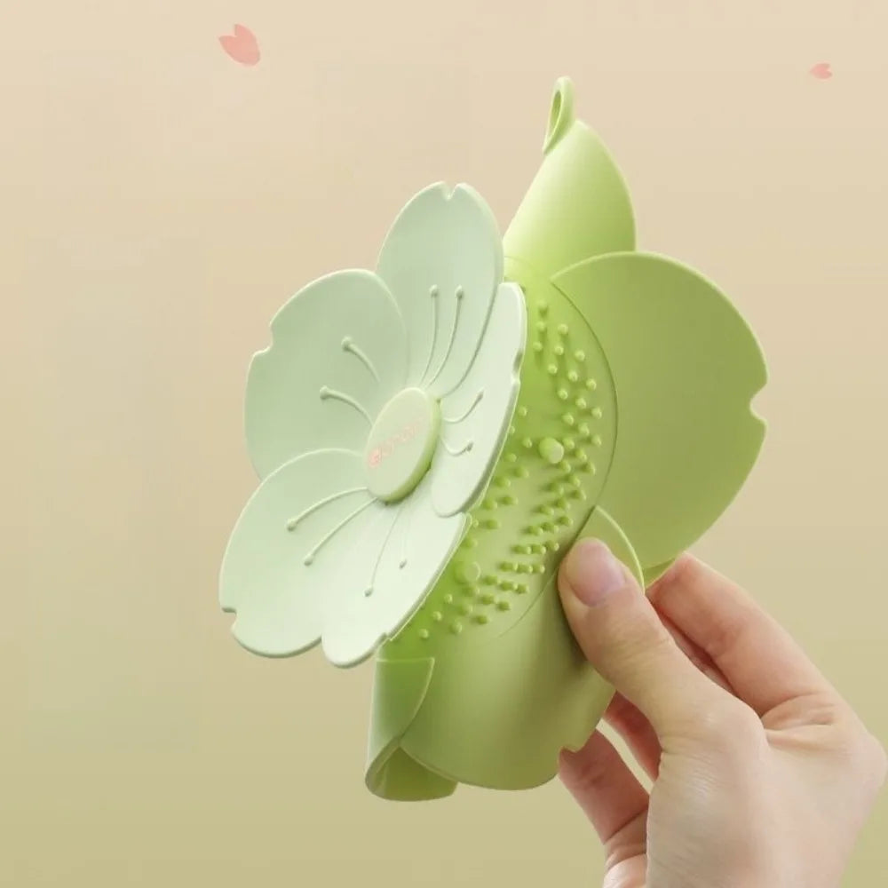 Hand holding a green silicone drain cover for bathroom shaped like a flower with soft petals