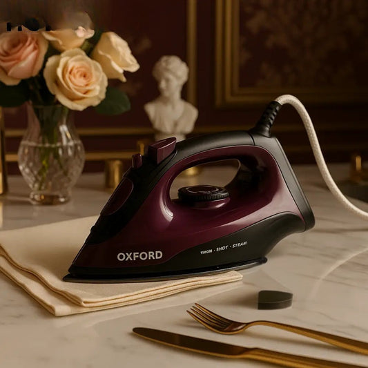 Oxford Deluxe steam iron in dark red and black resting on beige cloth on a marble table with roses and decorative items in the background