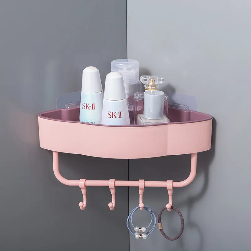 Pink wall-mounted corner shower shelf with hooks holding skincare bottles and hair ties in bathroom corner