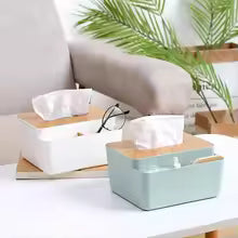 Plastic tissue box with wooden lid in white and green on a table beside a sofa with plants in background