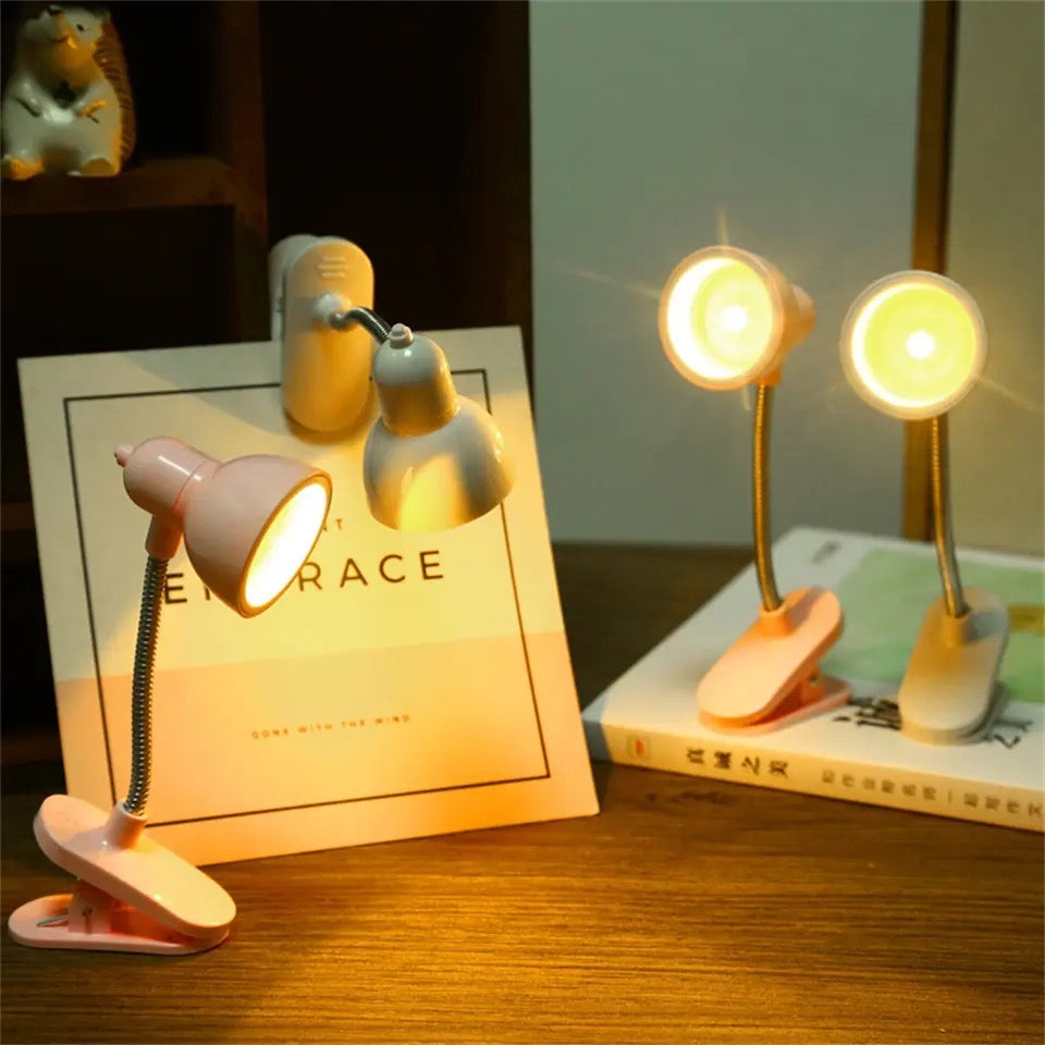 Portable book reading light clips in pink and white with flexible necks illuminating books on a wooden surface