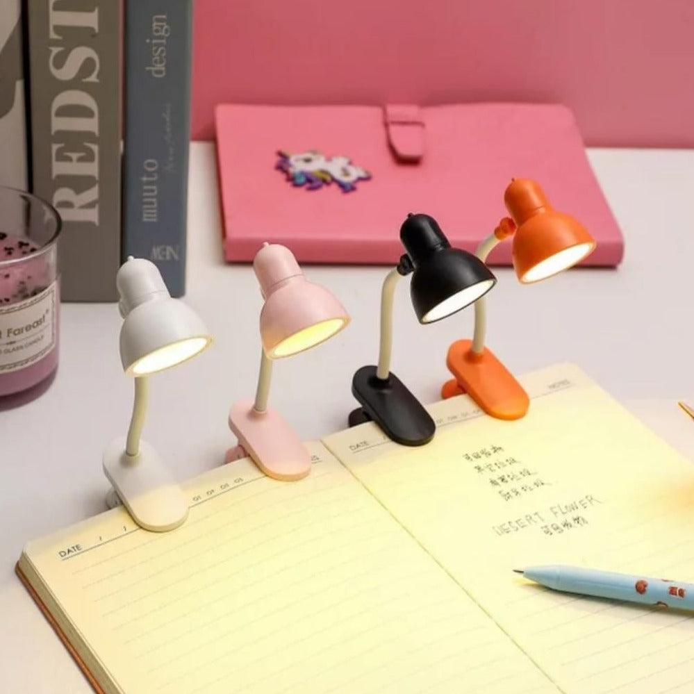 Set of four portable book reading light clips in white, pink, black, and orange illuminating open notebooks