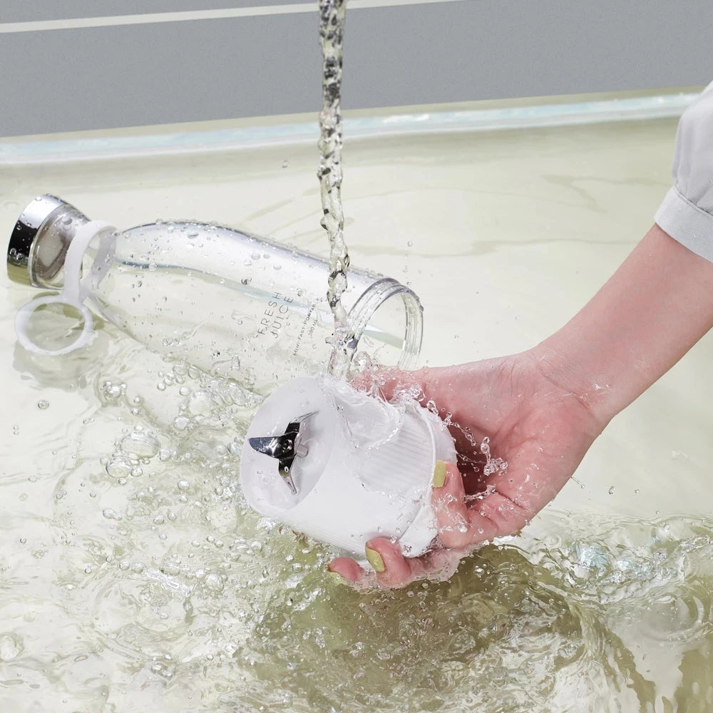 Hand washing portable electric juicer blender blade component under running water near clear detachable bottle