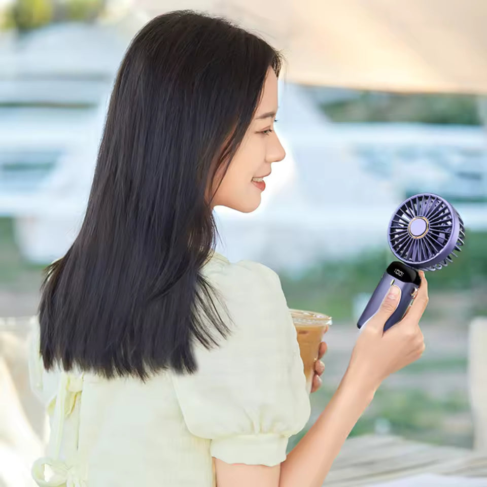 Woman holding a purple portable handheld fan rechargeable outdoors while drinking iced coffee