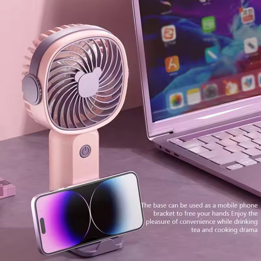 Portable mini fan USB rechargeable in pink with mobile phone holder next to laptop on desk