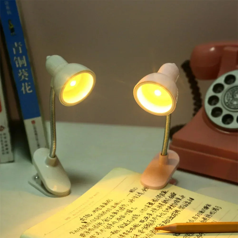 Two portable mini night light lamps with clip bases illuminating a book on a desk