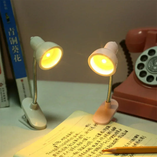 Two portable mini night light lamps with clip bases illuminating a book on a desk