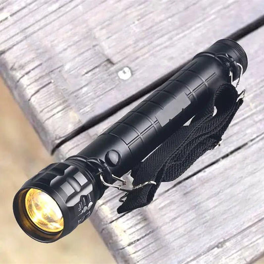 Black portable outdoor flashlight for camping with wrist strap resting on wooden surface
