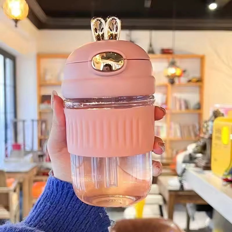 Portable rabbit water bottle in pink with gold bunny ears held in hand for easy carrying