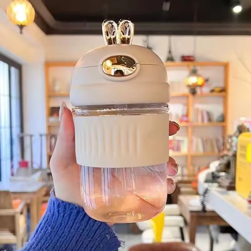Clarify.pk portable rabbit water bottle in beige held by hand with ribbed grip and gold bunny ears lid