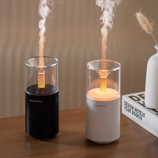 Black and white portable USB aroma humidifier emitting mist on a wooden table next to a white vase and book