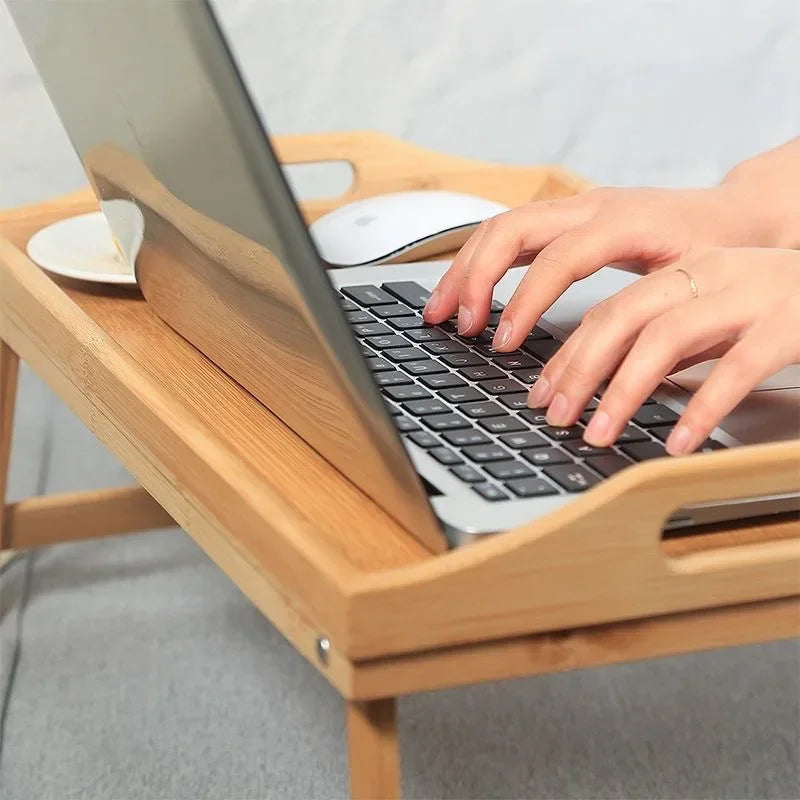 Hands typing on laptop placed on premium quality natural bamboo table with raised edges and foldable legs