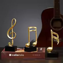 Resin musical note decor 3 pieces set in gold finish on black stands displayed on a book with guitar background