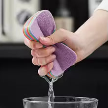 Person squeezing water out of purple reusable dishcloths for kitchen over a glass bowl