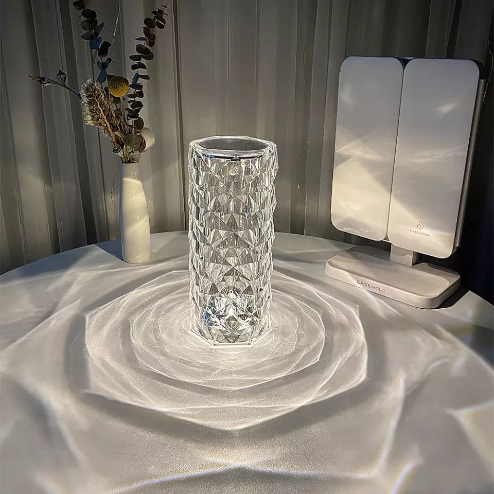 Rose crystal rechargeable lamp casting patterned light on a white surface with a vase and a white device nearby
