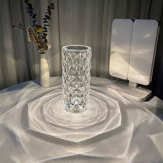 Rose crystal rechargeable lamp casting patterned light on a white surface with a vase and a white device nearby