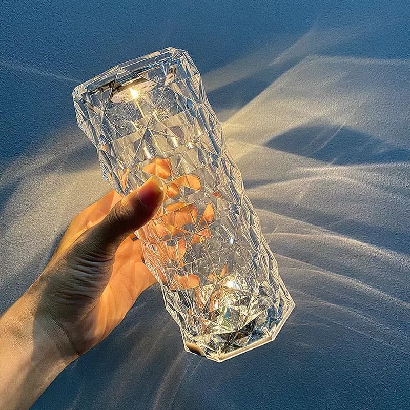 Hand holding a clear geometric rose crystal rechargeable lamp casting light patterns on a surface