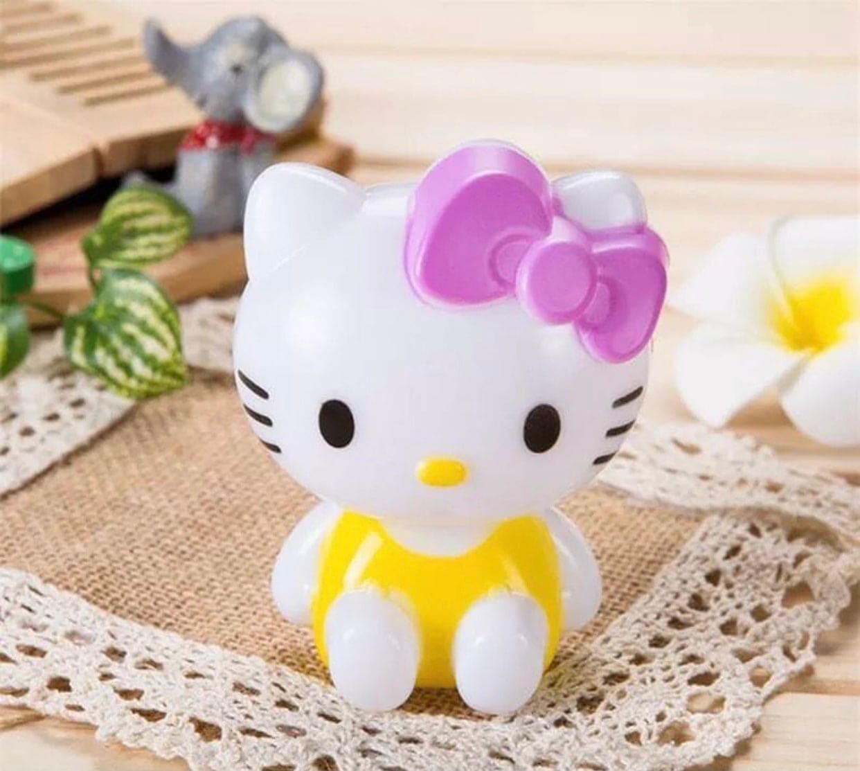 Hello Kitty night light with white face pink bow and yellow outfit sitting on a lace mat