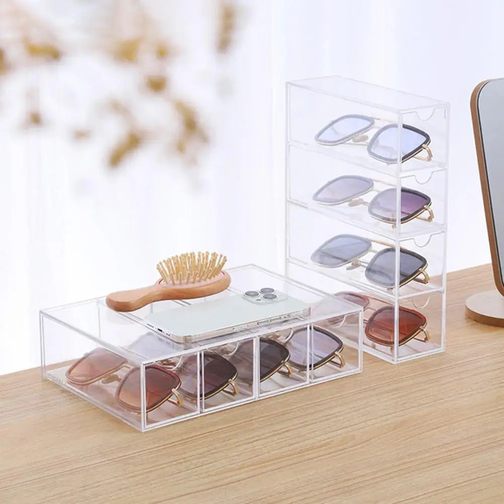 Clear acrylic sunglasses storage box with multiple compartments holding various sunglasses on wooden surface