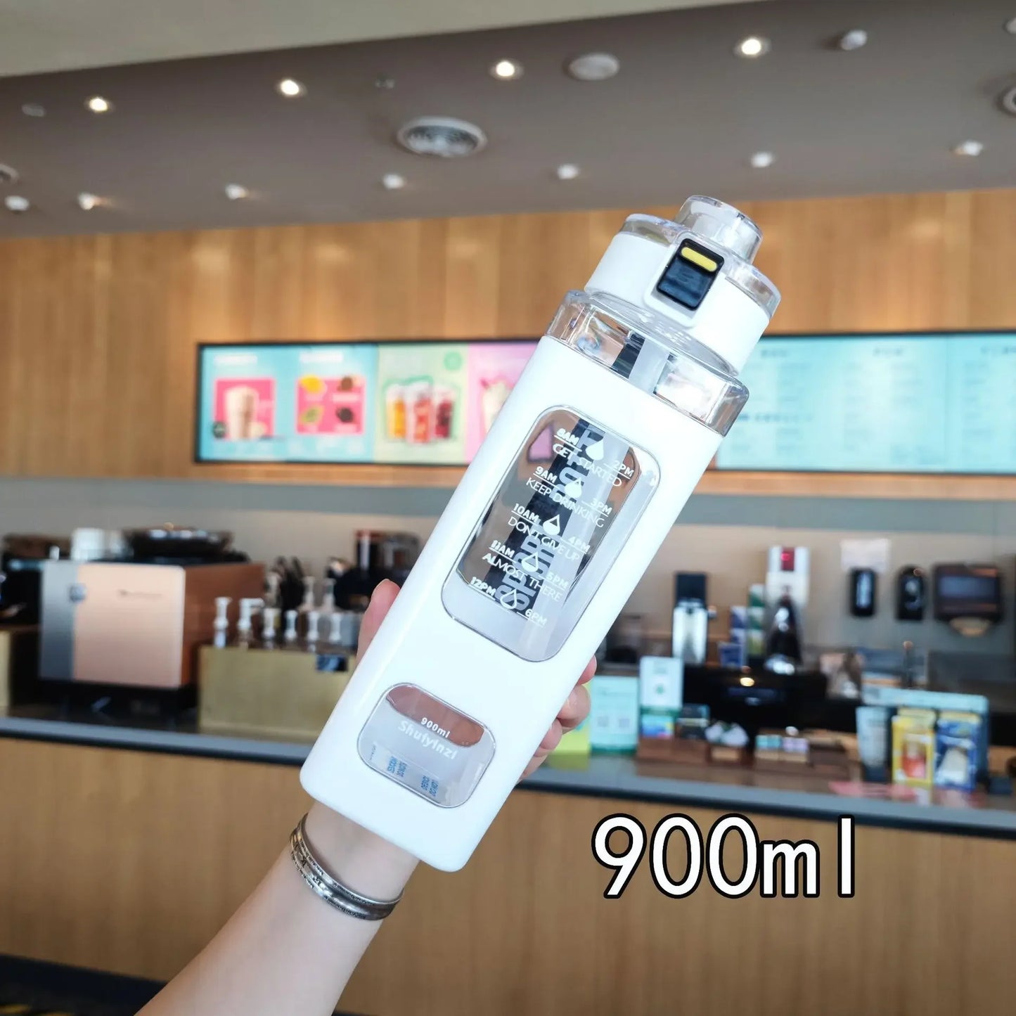 900ml leak proof water bottle held in hand with clear body and white protective sleeve in cafe setting