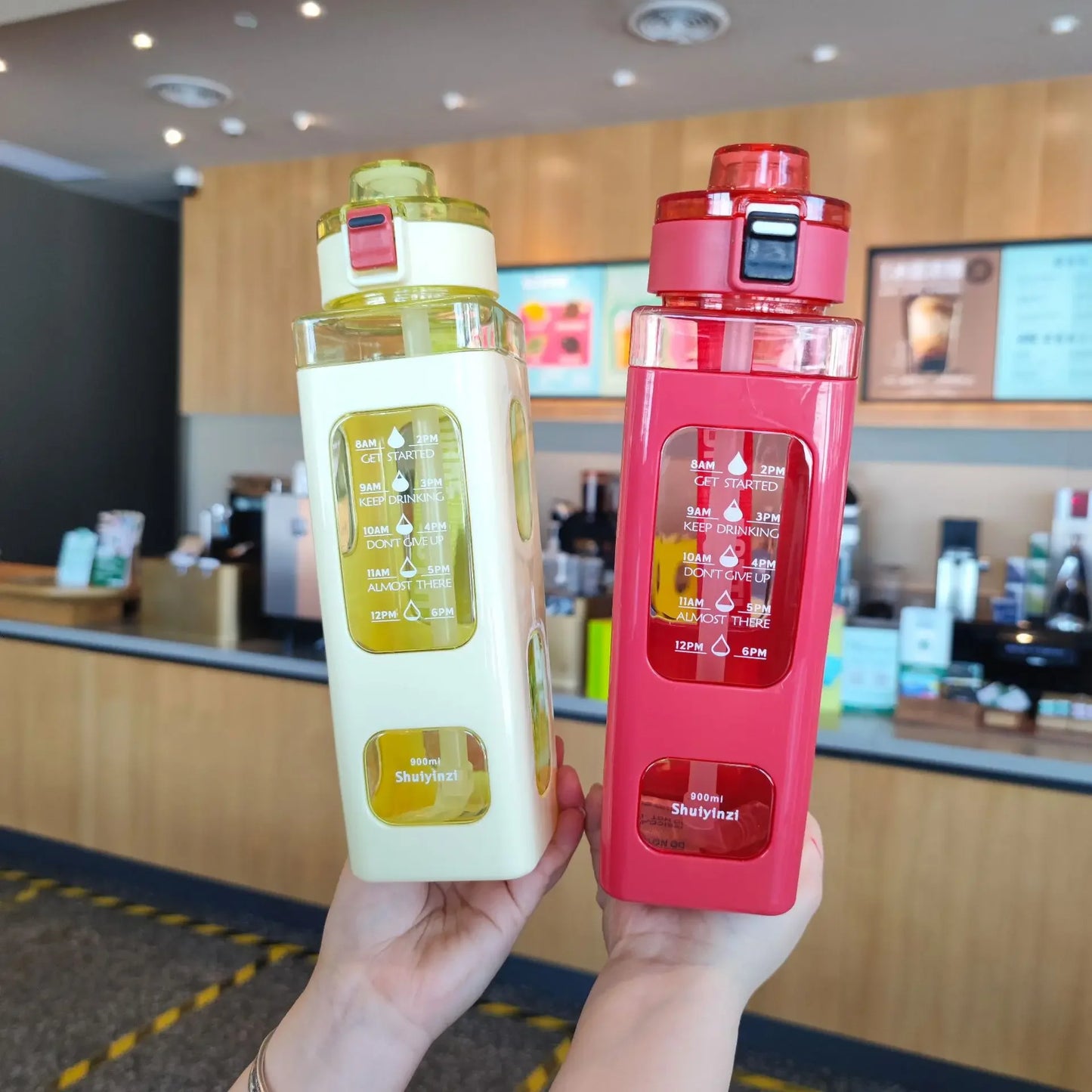 Clarify.pk 900ml leak proof water bottle in red and white colors held by hands in a cafe