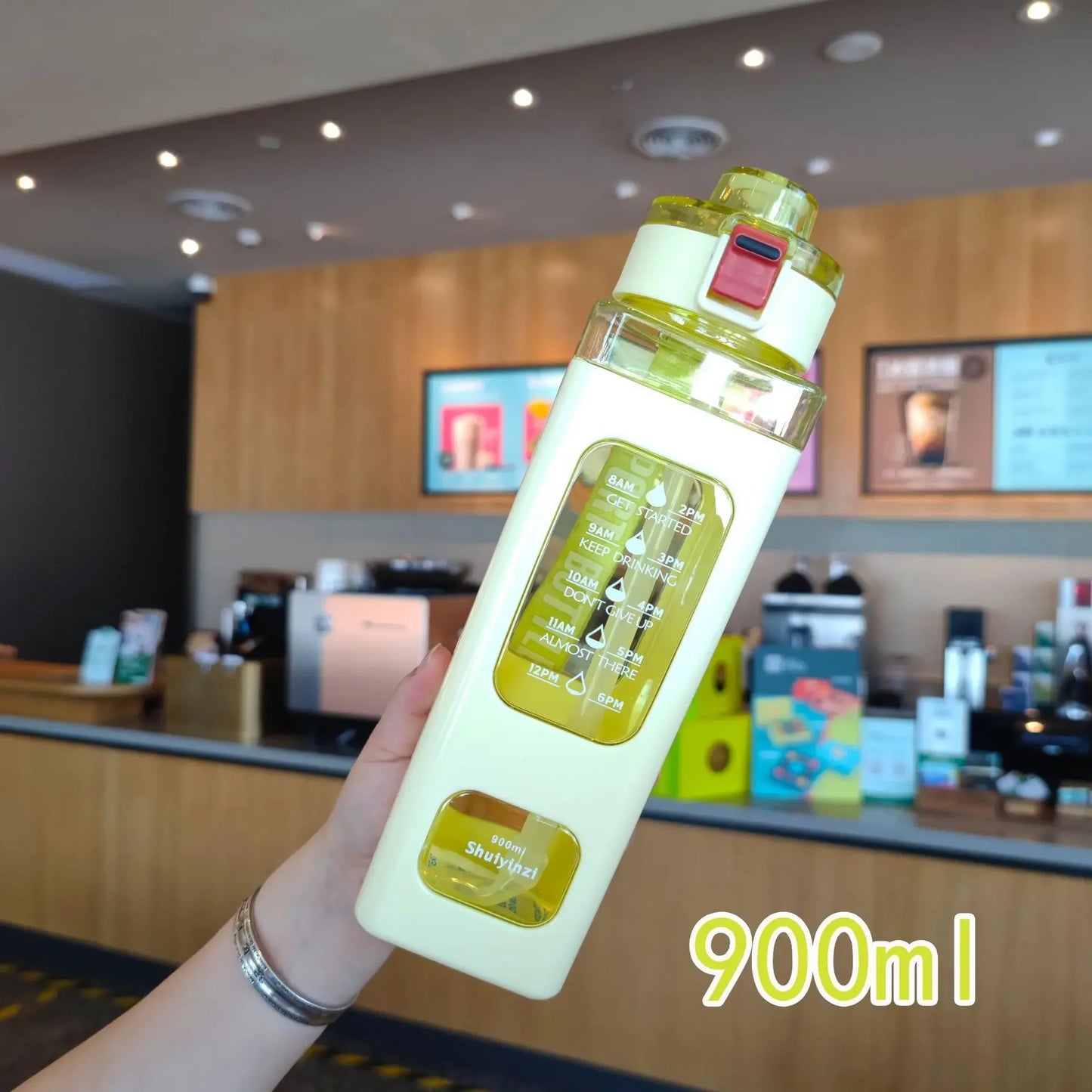 Hand holding a 900ml leak proof water bottle with yellow cap and measurement markings