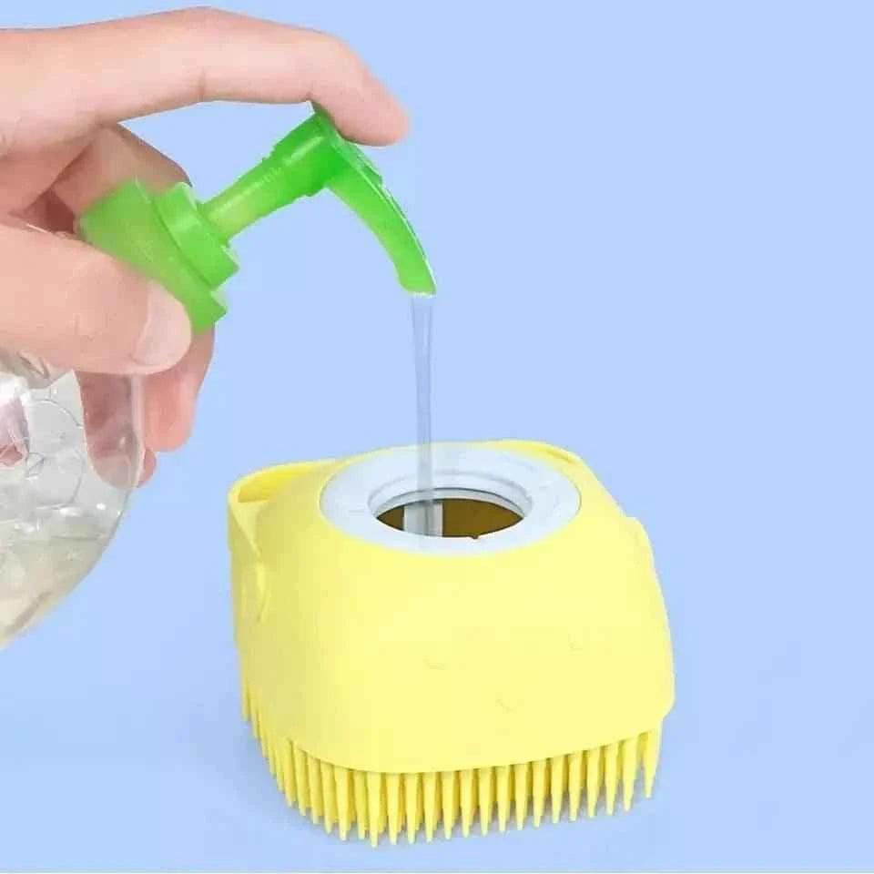 Yellow silicone baby bath brush with soft bristles being filled with liquid from green pump dispenser