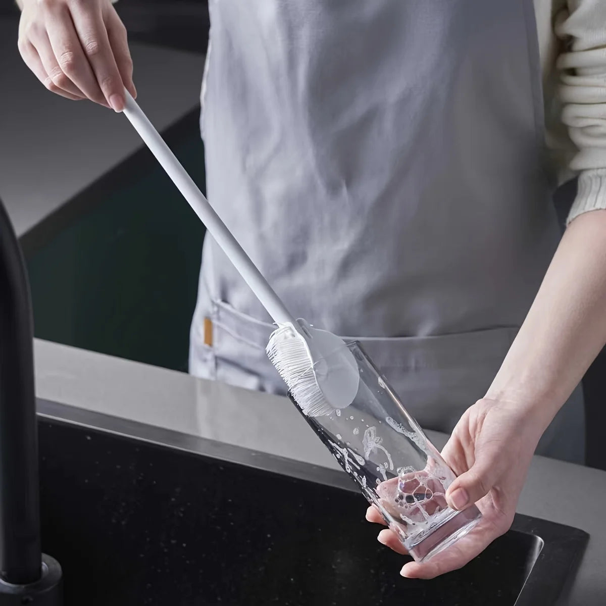 Person using a silicone bottle cleaning brush to clean a glass bottle in the kitchen sink