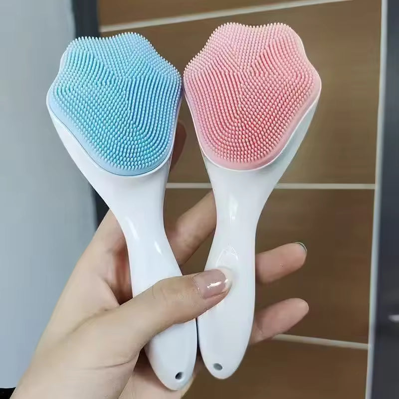 Hand holding two silicone facial cleansing brushes with soft bristles in blue and pink
